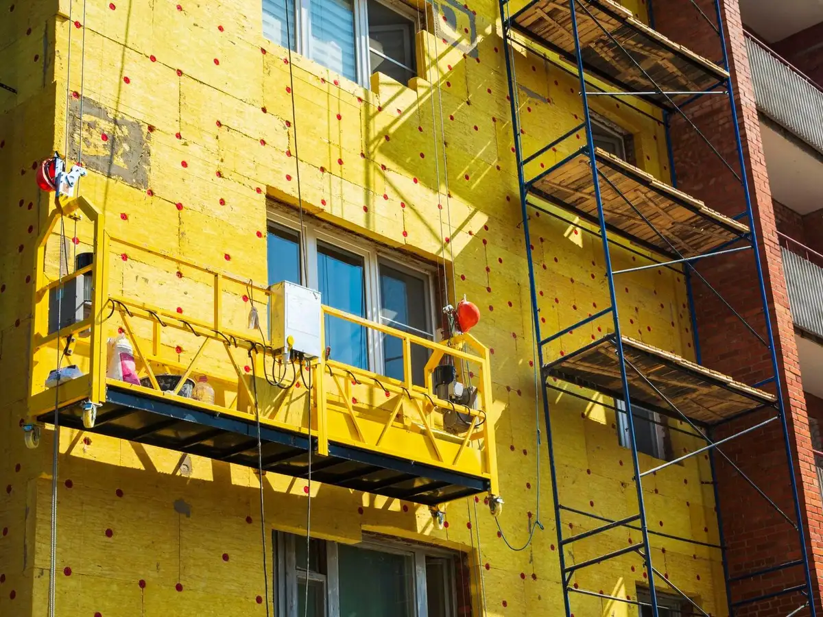 Panneaux d'isolation posés sur la façade d'un immeuble collectif depuis une nacelle et un échafaudage